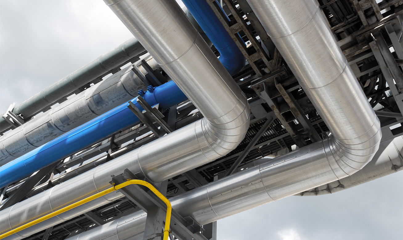 <h2>Travailler chez HERMETIC</h2> Industrial pipeline system with silver insulated pipes, blue and yellow pipes on a structural steel framework outdoors.