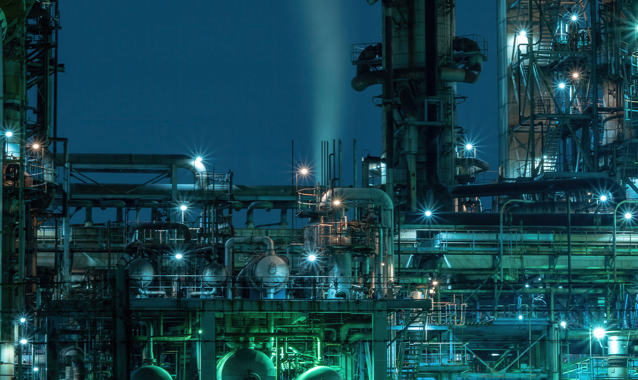 LNG/LPG industrial processing plant at night with illuminated pipes, towers, and vessels under a deep blue sky.
