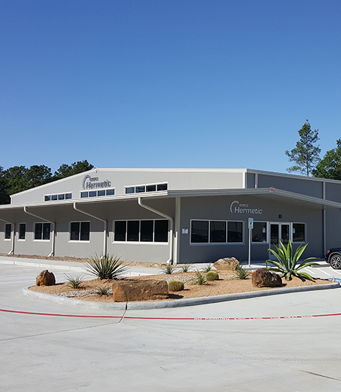<h3>Ouverture de la succursale aux États-Unis </h3> Modern HERMETIC company building with desert landscaping, cacti, and clear blue sky in Texas.