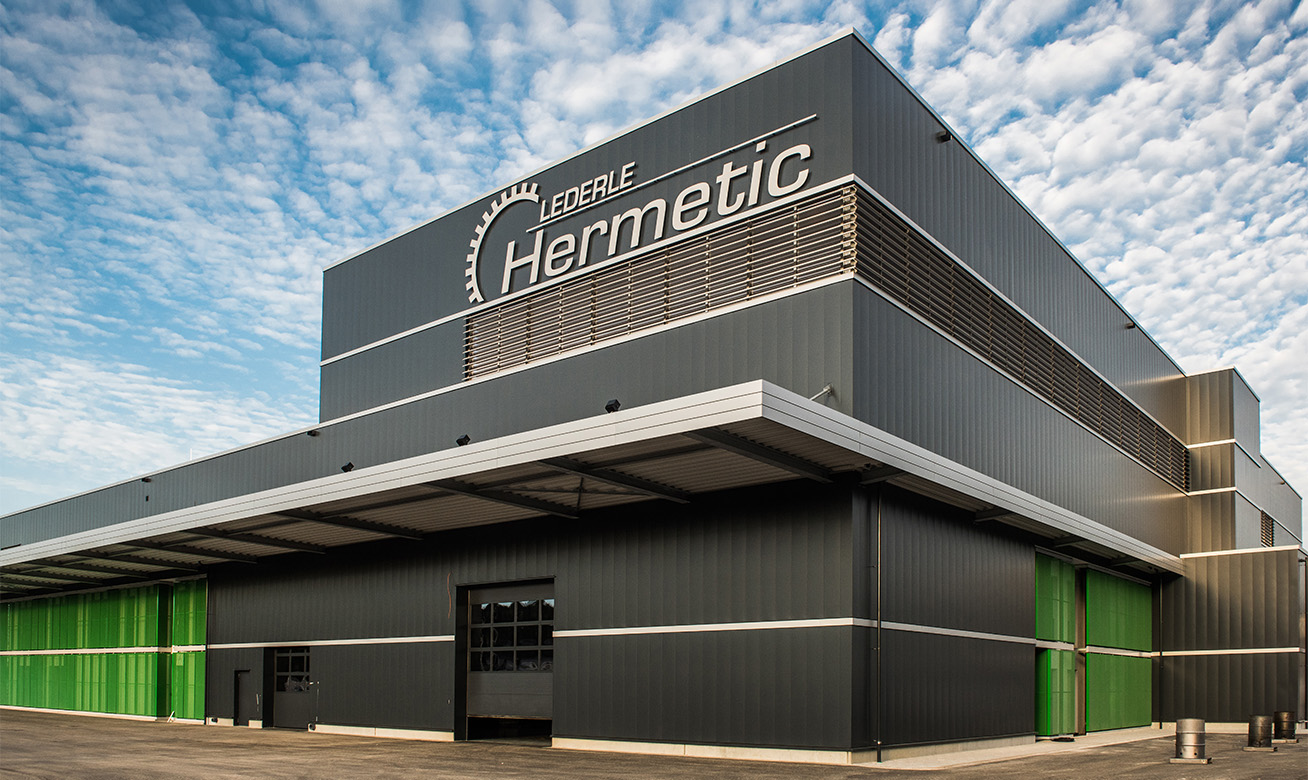 Exterior view of the Lederle HERMETIC industrial building with dark grey facade and green accents under a blue sky.