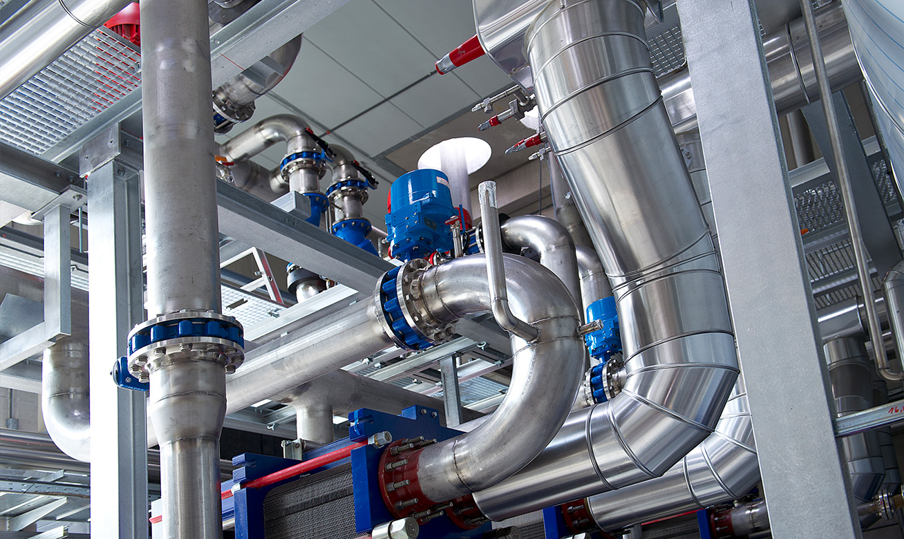 <h2>Travailler chez HERMETIC</h2> Industrial pipe system with stainless steel pipes, blue valves, and a heat exchanger in a modern facility.