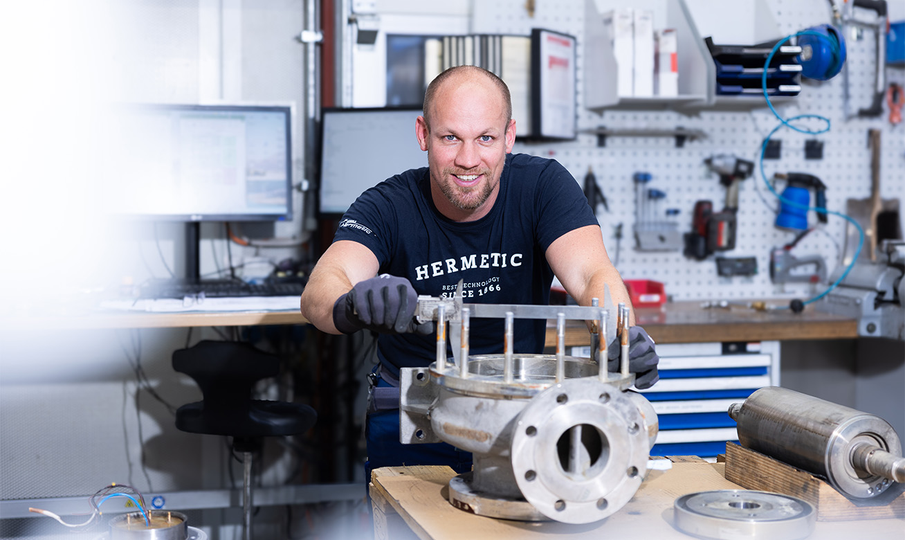 <h2>Les principales différences en un coup d'œil </h2> A technician in a HERMETIC t-shirt works on an industrial pump assembly in a well-equipped workshop.