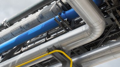<h3>Pompage d'huile caloporteuse pour le chauffage des réacteurs et des échangeurs thermiques</h3> Industrial pipeline system with insulated silver, blue, and yellow pipes on a steel support structure against cloudy sky.