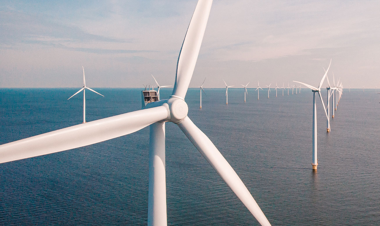 <h2>Solutions de pompage pour les circuits de refroidissement des éoliennes</h2> Offshore wind farm with rows of large white wind turbines standing in calm blue ocean water under a hazy sky.