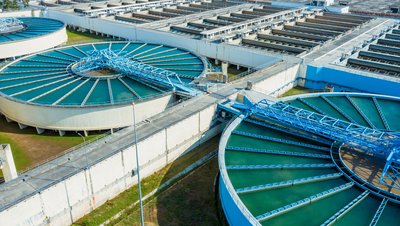 <h3>L'utilisation de la liqueur de potasse dans le traitement de l'eau</h3> Aerial view of a large water treatment plant with circular tanks and rectangular filtration basins filled with blue-green water.