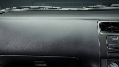 <h3>Fabricant de plastiques à base de styrène destinés à l'industrie automobile </h3> Dark grey car dashboard interior showing air vents, MODE and A/C control buttons, and textured plastic surface.