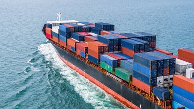 Aerial view of a large cargo container ship loaded with colorful shipping containers sailing across open ocean.