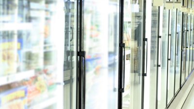 Row of glass-door refrigeration units in a supermarket, stocked with frozen food products.