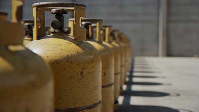 <h3>Reflux de propane dans une usine de GNL</h3> Row of yellow LPG gas cylinders lined up against a concrete wall, casting shadows on the ground.