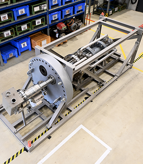 <h3>La plus grande pompe à rotor noyé au monde </h3> Large industrial machine assembly mounted on a steel frame, photographed in a manufacturing facility warehouse.