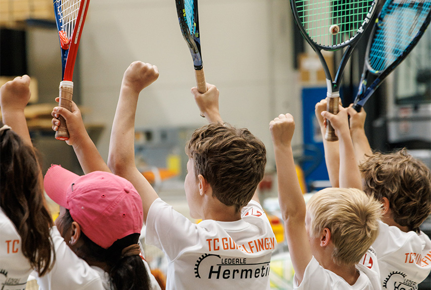 Children from TC Gundelfingen raising tennis rackets in celebration, wearing white club shirts sponsored by Lederle HERMETIC.