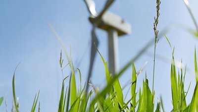 <h3>Refroidissement des onduleurs dans les éoliennes </h3> Wind turbine rising above lush green grass against a clear blue sky, symbolizing renewable energy