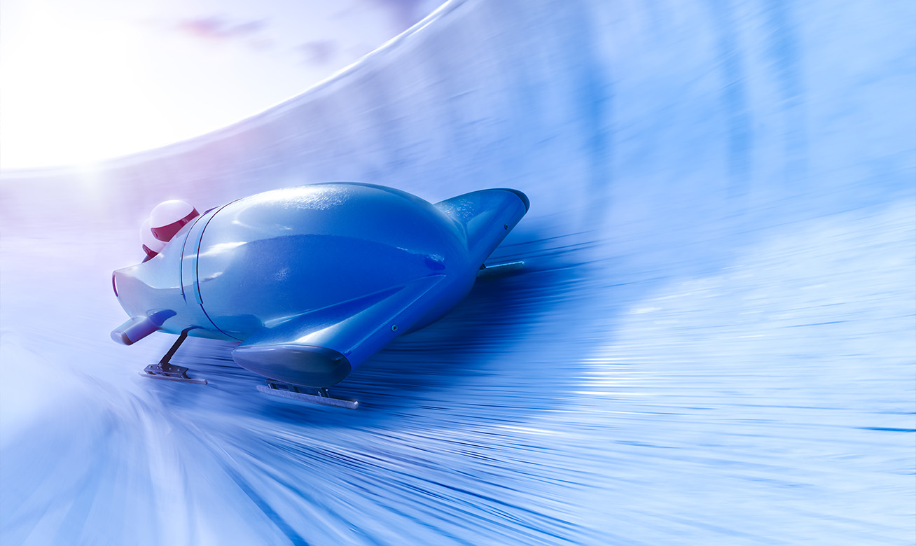 <h2>Travailler chez HERMETIC</h2> A blue bobsled races at high speed down an icy track, with motion blur conveying intense velocity.