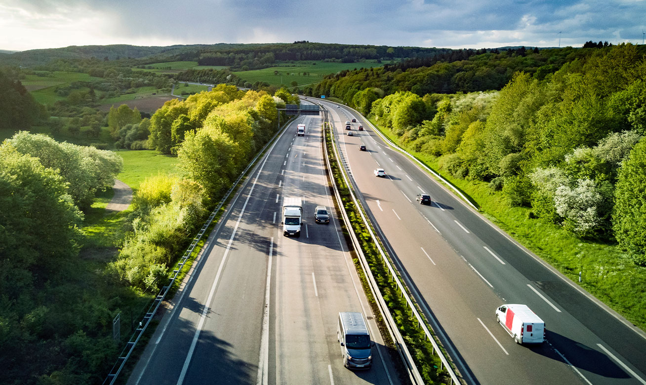 <h2>Manipulation en toute sécurité des fluides réactifs dans la production de matières plastiques</h2> Aerial view of a dual carriageway highway surrounded by lush green forests and rolling hills, with cars and trucks in traffic.