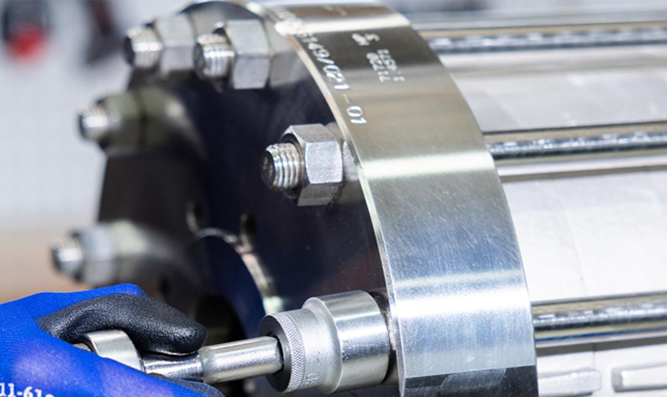 Gloved hand using a socket wrench to tighten bolts on a polished metal industrial flange assembly.