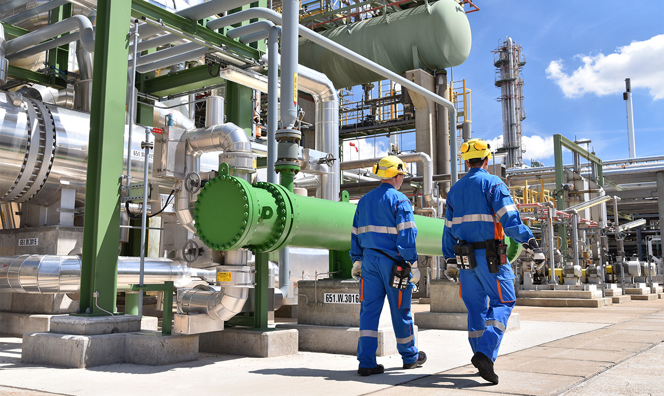 <h2>Qu'est-ce que la protection contre les explosions (protection Ex) ?</h2> Two workers in blue coveralls and yellow hard hats inspecting pipelines at an industrial chemical plant facility.