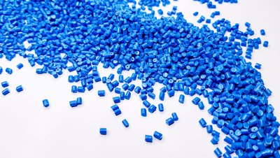 Blue plastic pellets/granules scattered on white surface, used in aromatics, solvents and amines applications.